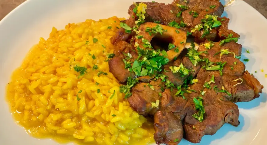 Un piatto invitante di risotto giallo cremoso accanto a un ossobuco tenero, guarnito con prezzemolo fresco e scorza di limone.