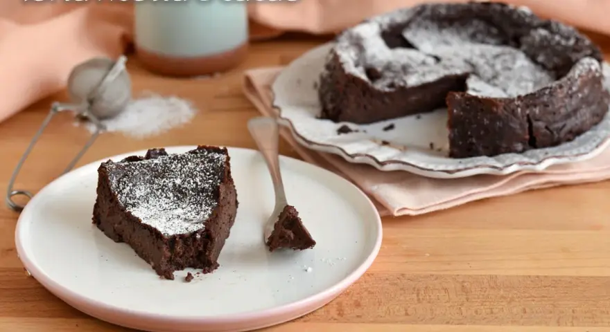 Una fetta di torta ricotta e cioccolato senza farina, cosparsa di zucchero a velo, su un piatto bianco.
