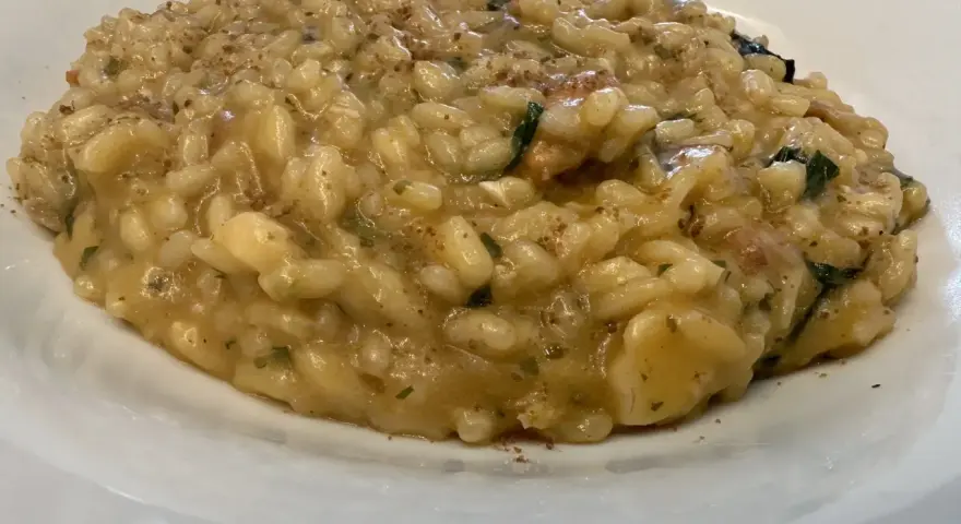 Un cremoso risotto alla pescatora ricetta napoletana, con riso carnaroli e profumi di mare, servito in un piatto bianco.