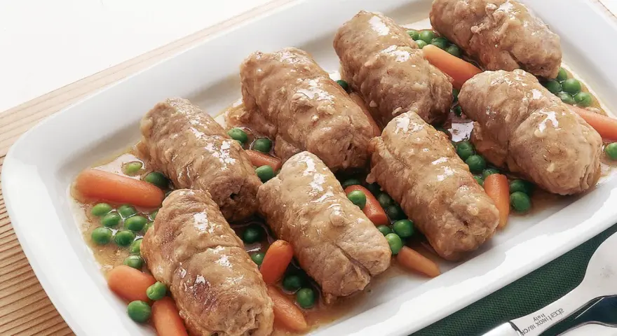 Involtini di carne succulenti serviti con carote e piselli in un piatto bianco.