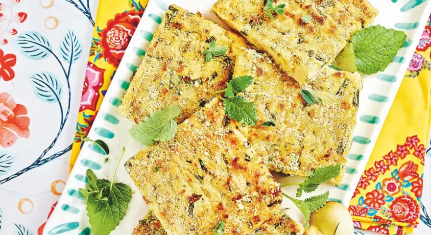 Fette dorate di polpettone di fagiolini, guarnite con erbe aromatiche fresche, su un piatto decorato con motivi floreali vivaci.