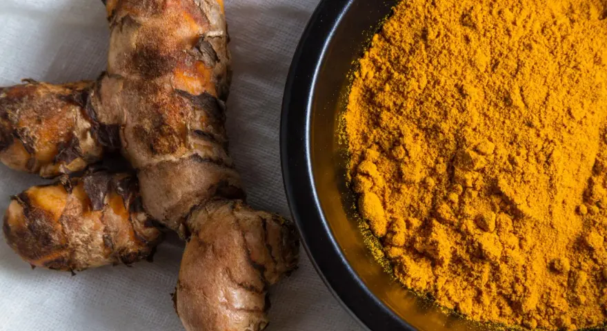 Radici di curcuma e polvere dorata in una ciotola, perfette per dare colore e sapore alla pasta.
