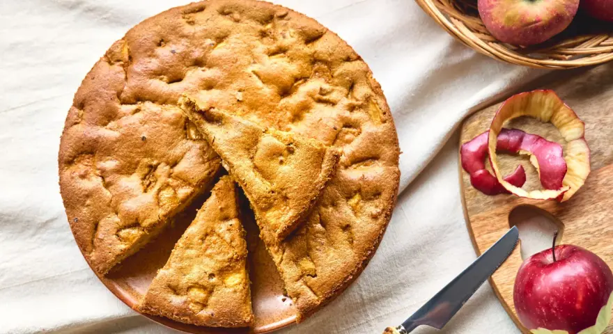 Una deliziosa torta di mele con farina di avena, appena sfornata, con mele fresche e scorze su un tagliere.