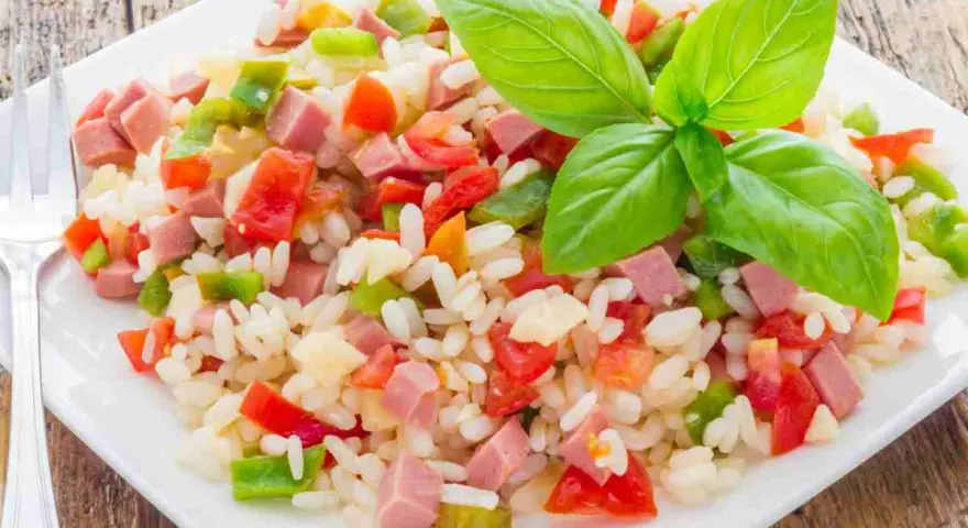 Un colorato insalata di riso con cubetti di prosciutto, peperoni e pomodori, guarnita con foglie di basilico fresco.