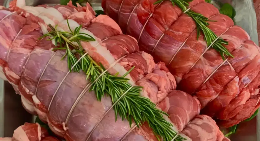Due **tagli di carne per arrosto** pronti per essere cucinati, legati con spago e guarniti con rametti di rosmarino fresco.