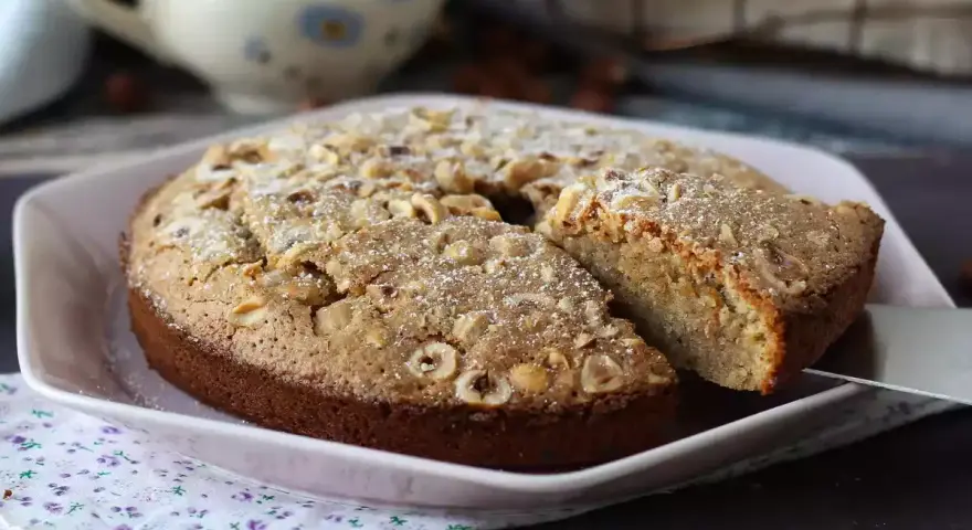 Deliziosa torta di nocciole senza farina, cosparsa di zucchero a velo e nocciole intere. Perfetta per ogni occasione.