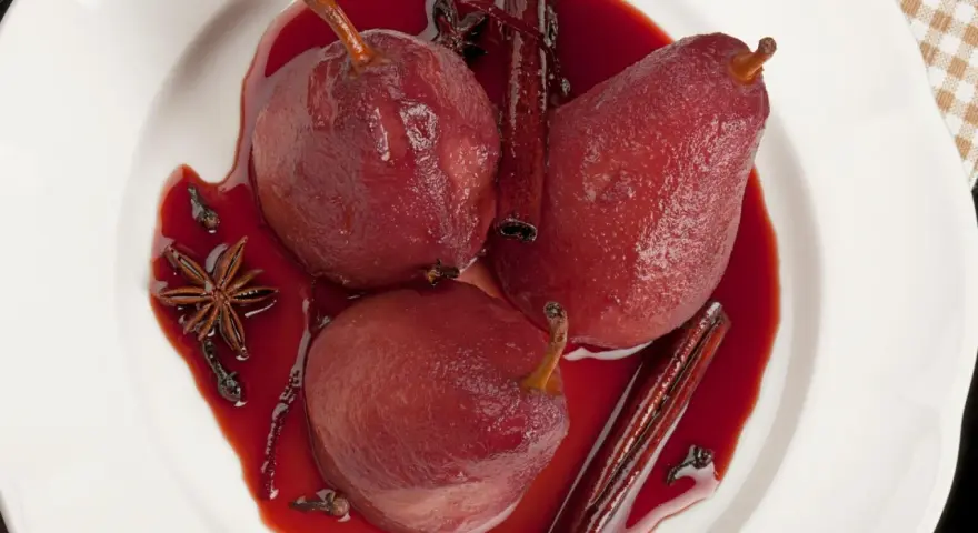 Pere cotte nel vino, profumate con cannella, anice stellato e chiodi di garofano, servite in una ciotola bianca.