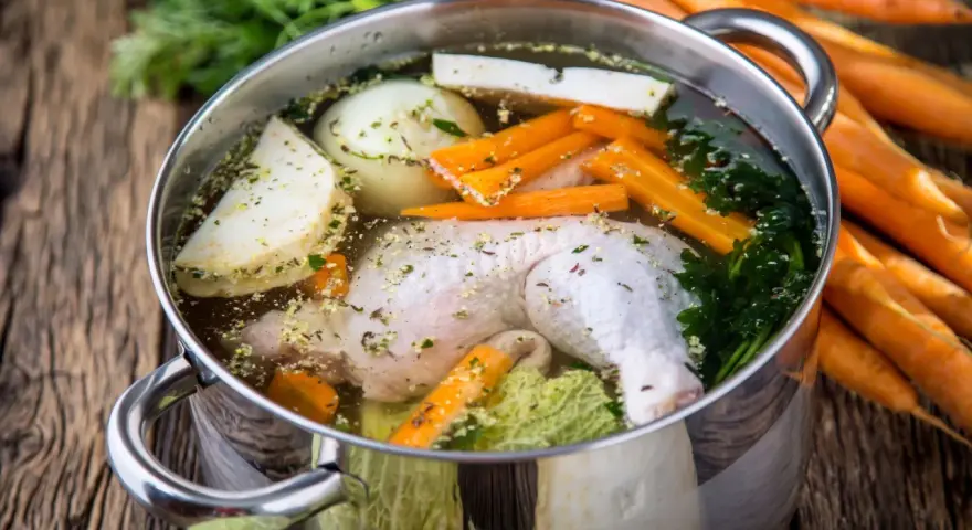 Brodo di pollo in pentola a pressione con carote, cipolla, sedano e prezzemolo.
