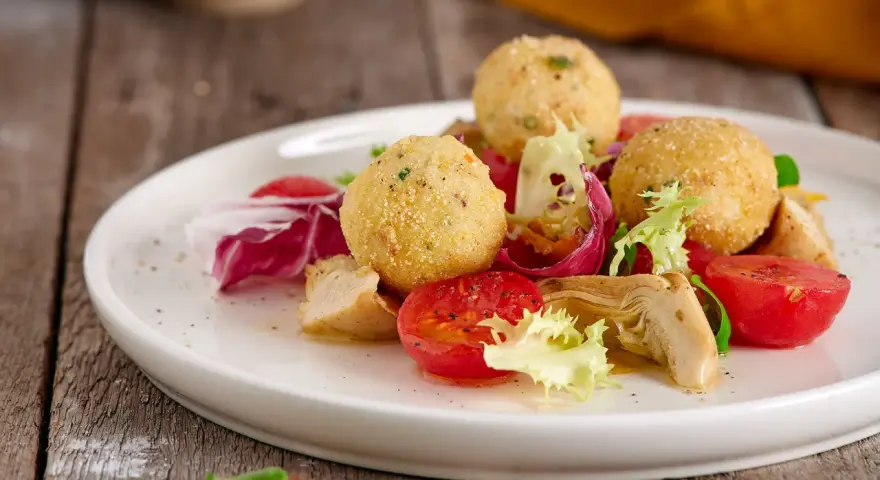 Sfere dorate di miglio fritte, servite con un'insalata fresca di pomodorini, radicchio e pollo. Un'idea gustosa per le tue ricette con miglio.