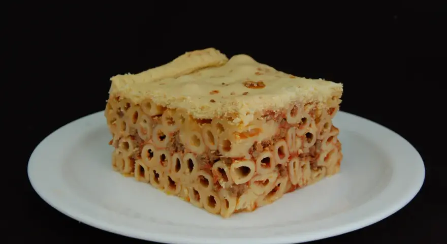 Un pezzo di timballo di pasta con ragù e pasta cotta al forno, servito su un piatto bianco.