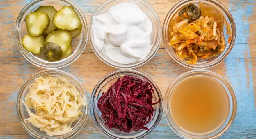 Sei ciotole di vetro con cetrioli, yogurt, kimchi, crauti, barbabietole e brodo, ingredienti per probiotici naturali fatti in casa.