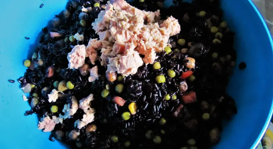 Un'insalata di riso nero con tonno, piselli e cubetti di pomodoro. La cottura del riso nero è perfetta, ogni chicco è ben separato.
