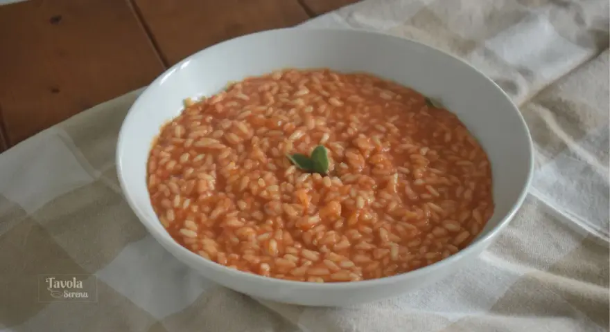 Un cremoso riso al pomodoro veloce, guarnito con una fogliolina verde, servito in una ciotola bianca su una tovaglia a quadri.