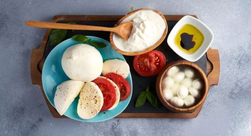 La differenza tra burrata e mozzarella è evidente: la burrata cremosa in ciotola, la mozzarella fresca su piatto con pomodoro.