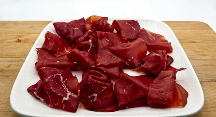 Fette di bresaola, la bresaola che carne è, su un piatto bianco.
