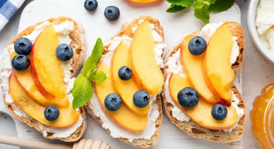 Bruschette con pesche mature, ricotta e mirtilli. Un'idea fresca per ricette con pesche mature, perfetta per la colazione o uno spuntino leggero.