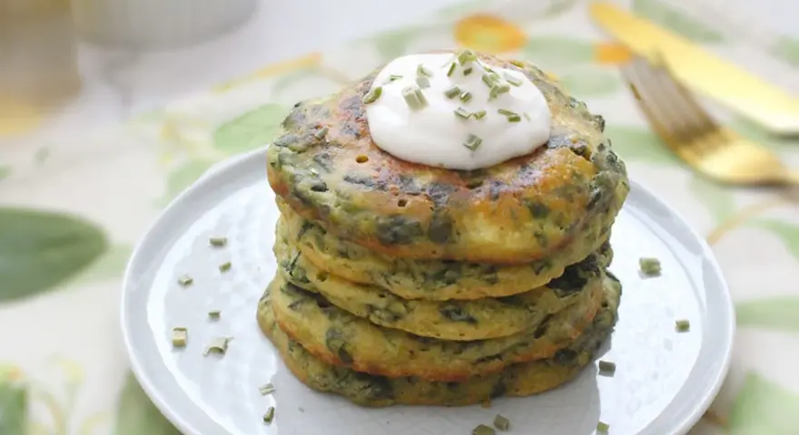 Pancakes salati con farina di grano saraceno e spinaci, guarniti con panna acida e erba cipollina. Un'idea gustosa per le tue ricette con farina di grano saraceno.