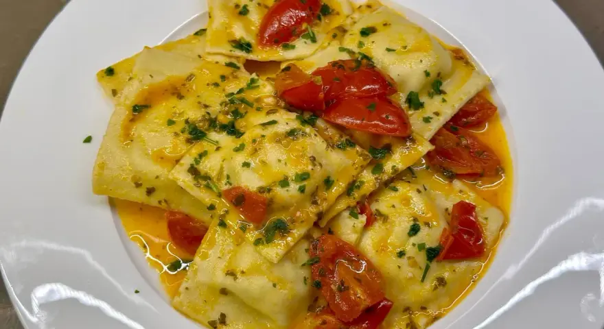 Deliziosi ravioli di pesce conditi con pomodorini e prezzemolo, in un sugo dorato.