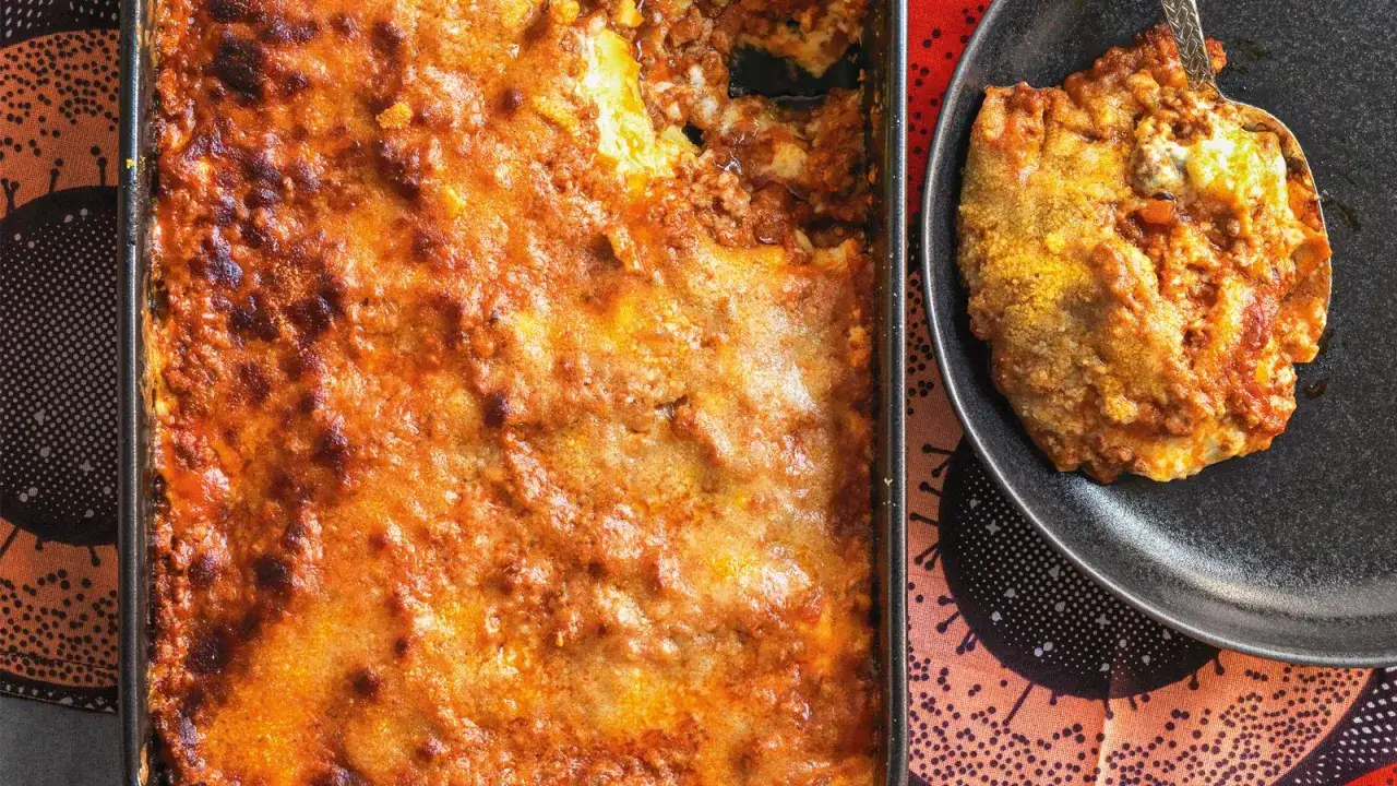 Lasagna al ragù appena sfornata, dorata e invitante, con una porzione servita su un piatto scuro.