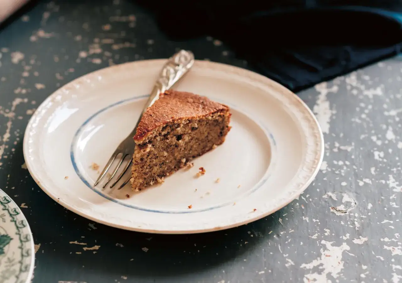 Una fetta di torta di nocciole senza farina, umida e profumata, su un piatto bianco con forchetta.