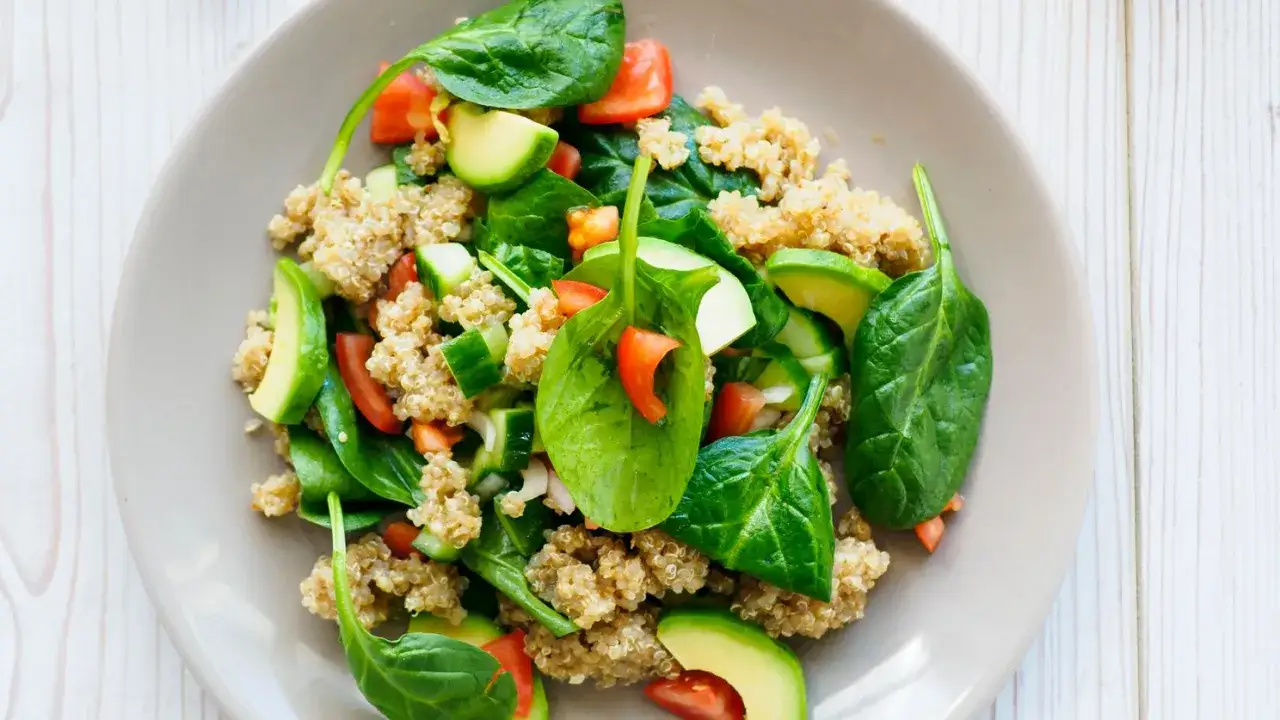 Insalata colorata con quinoa, spinaci freschi, pomodori, cetrioli e avocado. Un'idea sana su come cucinare gli spinaci in modo gustoso.
