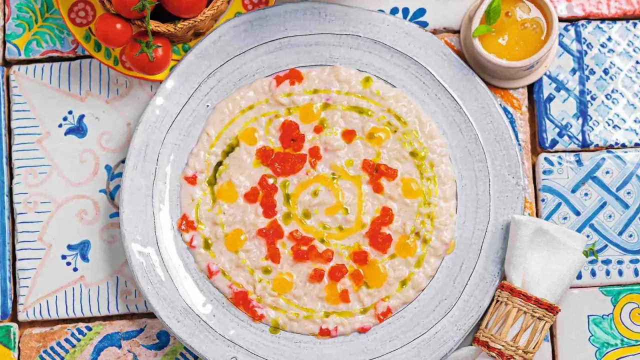 Un cremoso riso al pomodoro veloce, guarnito con pomodorini freschi e un filo d'olio d'oliva, su un piatto decorato con maioliche colorate.