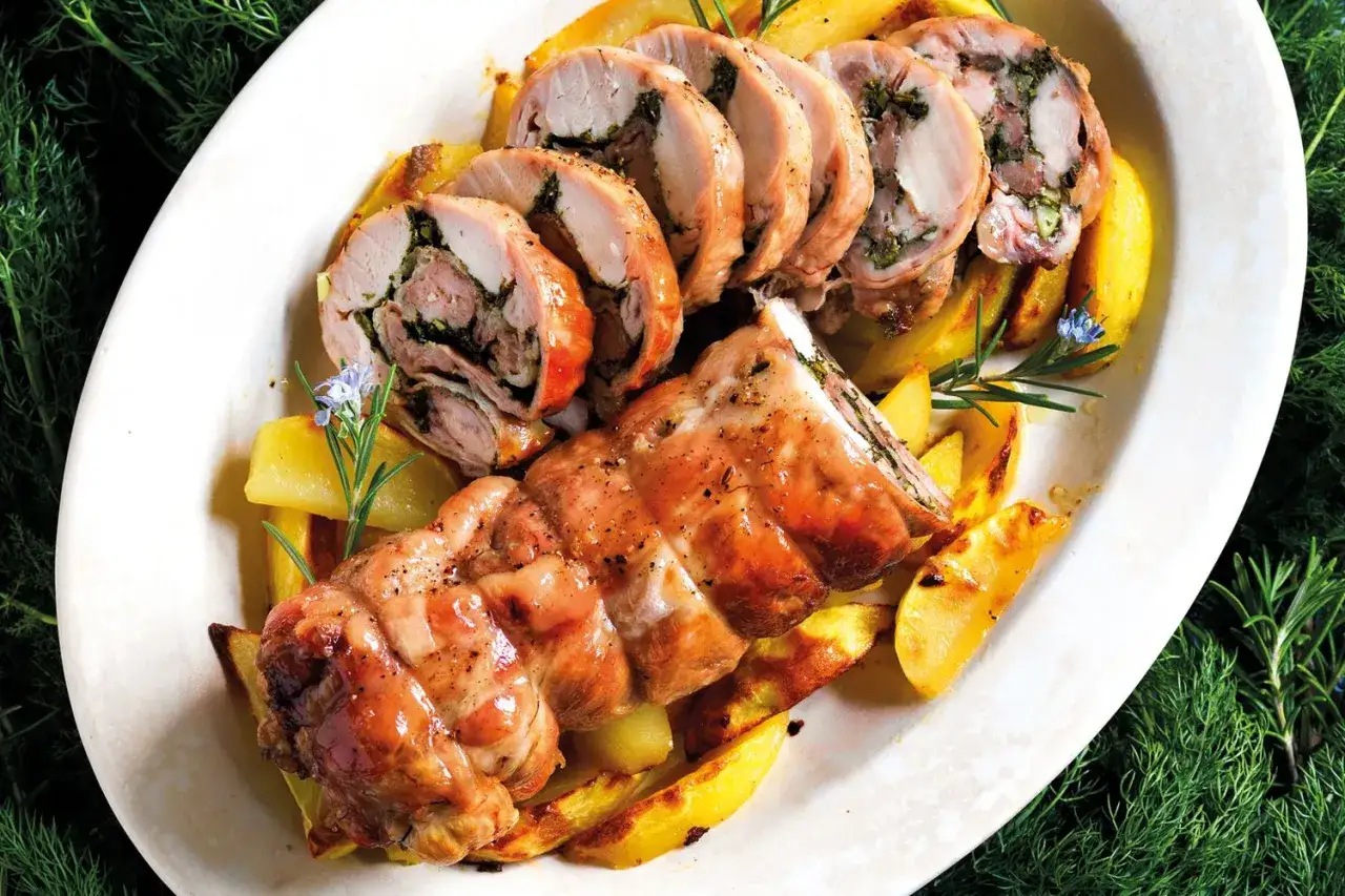 Coniglio in porchetta, un arrosto succulento farcito con erbe aromatiche, servito su patate dorate e guarnito con rosmarino e fiori.