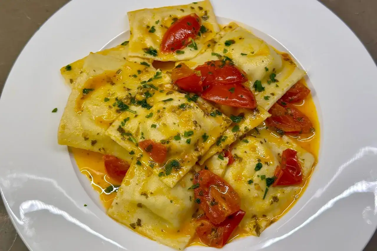 Deliziosi ravioli di pesce conditi con pomodorini e prezzemolo, immersi in una salsa dorata.