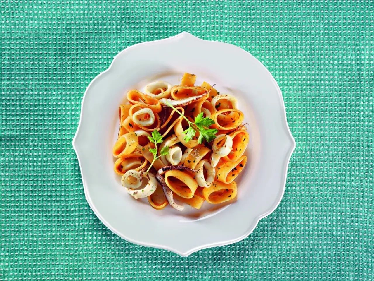 Piatto di calamarata con calamari freschi, pomodoro e prezzemolo. Un classico su come si fa la calamarata.