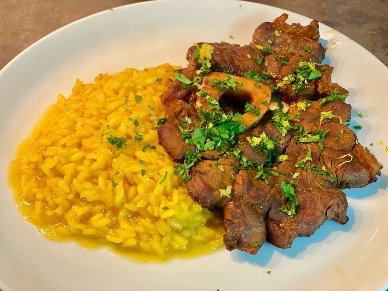 Un invitante risotto giallo brillante accanto a un succulento ossobuco, guarnito con prezzemolo fresco.