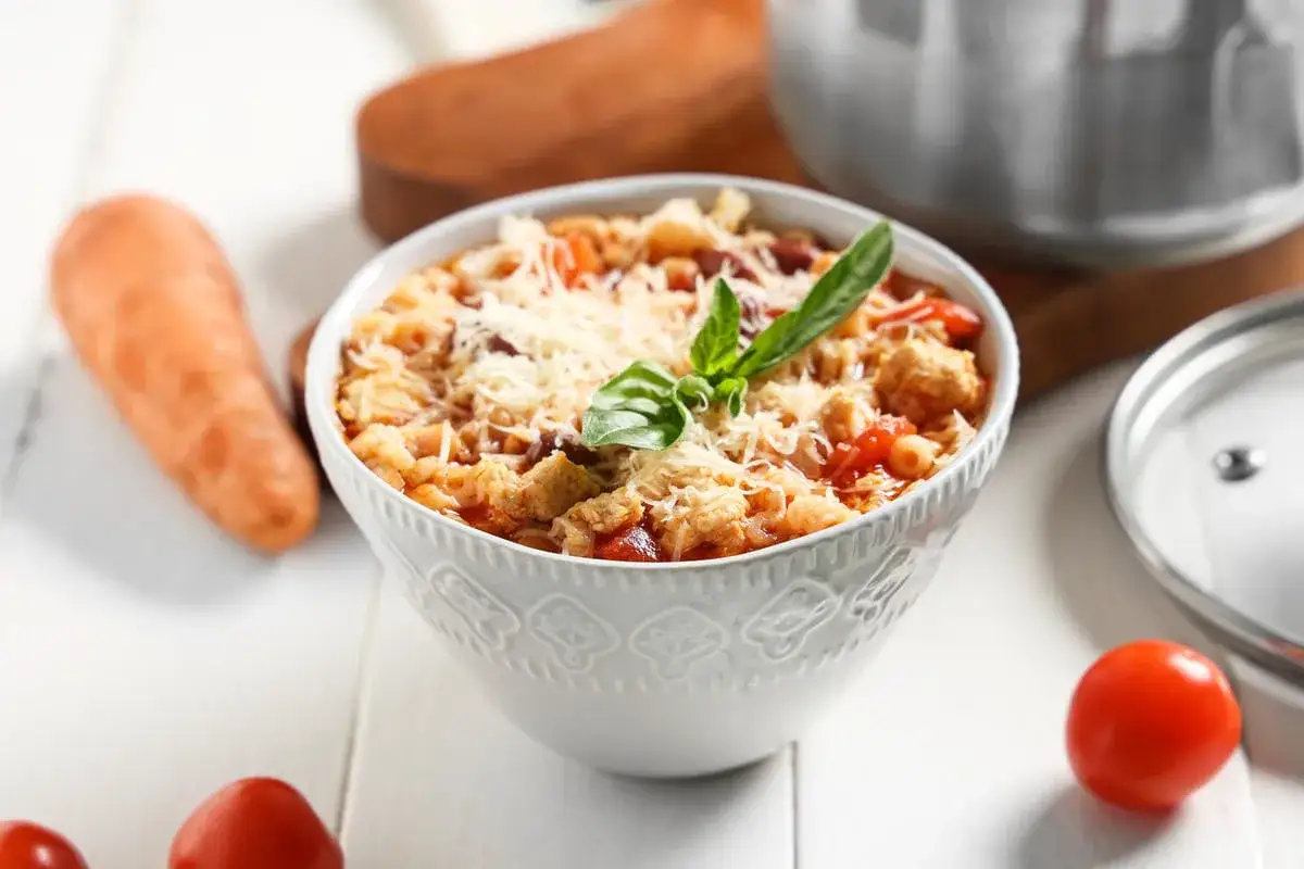 Una ciotola di pasta e fagioli estiva, ricca e saporita, guarnita con parmigiano e basilico. Ingredienti freschi come carote e pomodori completano la scena.