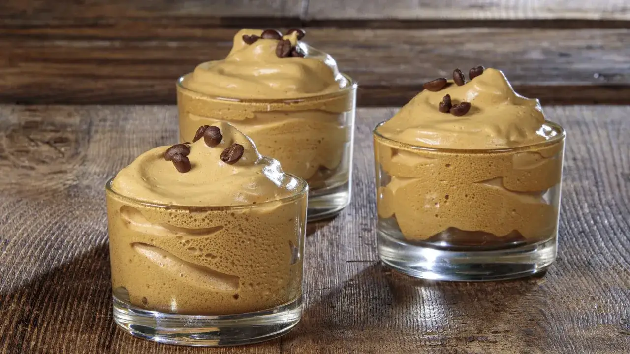 Tre bicchierini di crema di caffè montata, guarniti con chicchi di caffè, perfetti per chi vuole imparare come fare la crema di caffè.