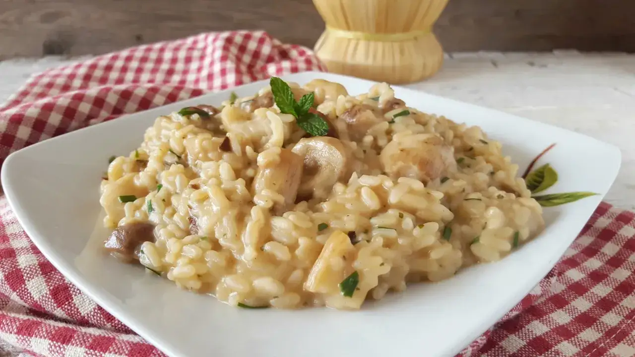 Un cremoso risotto ai funghi surgelati, guarnito con menta fresca, servito su un piatto bianco con tovagliolo a quadri rossi.