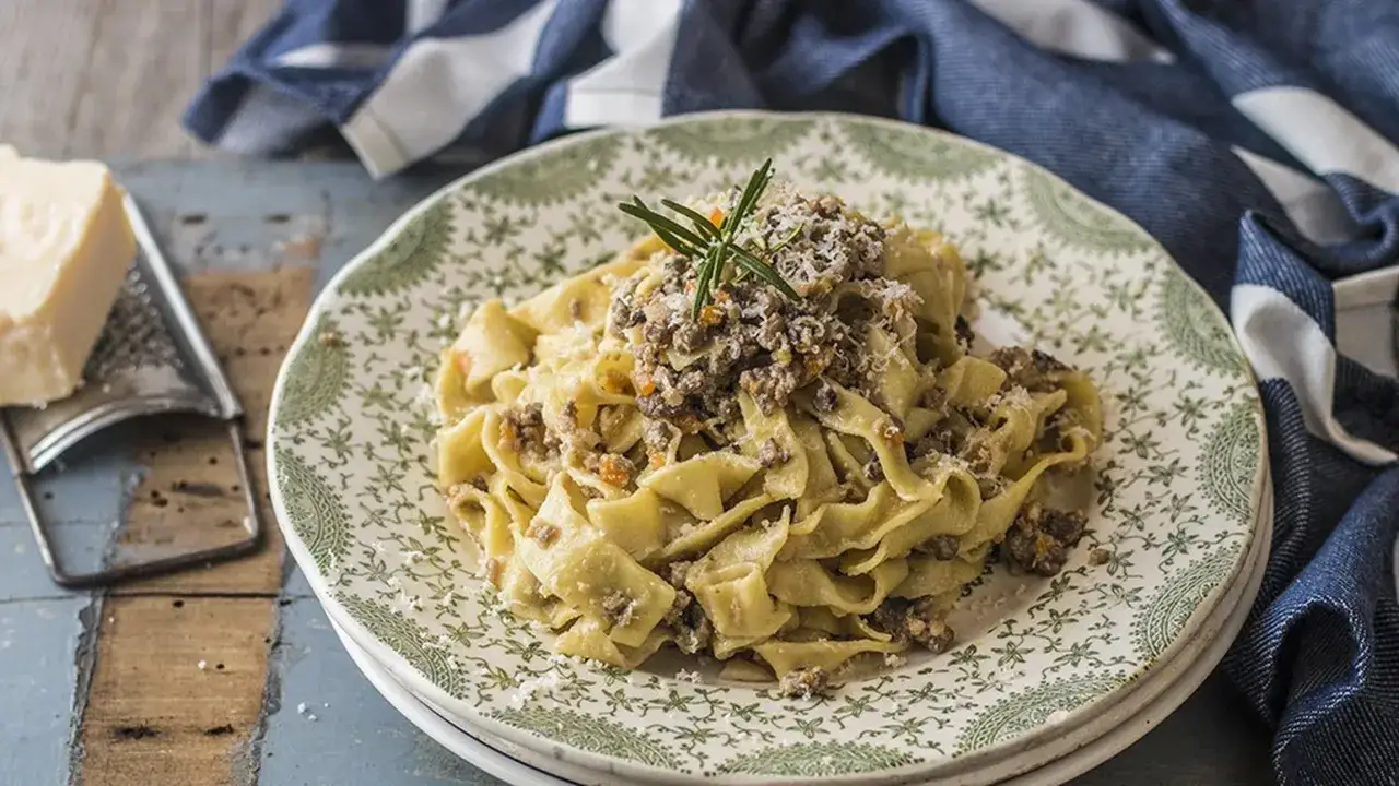 Piatto di pappardelle condite con un saporito ragù di cinghiale in bianco, guarnito con rosmarino e parmigiano grattugiato.