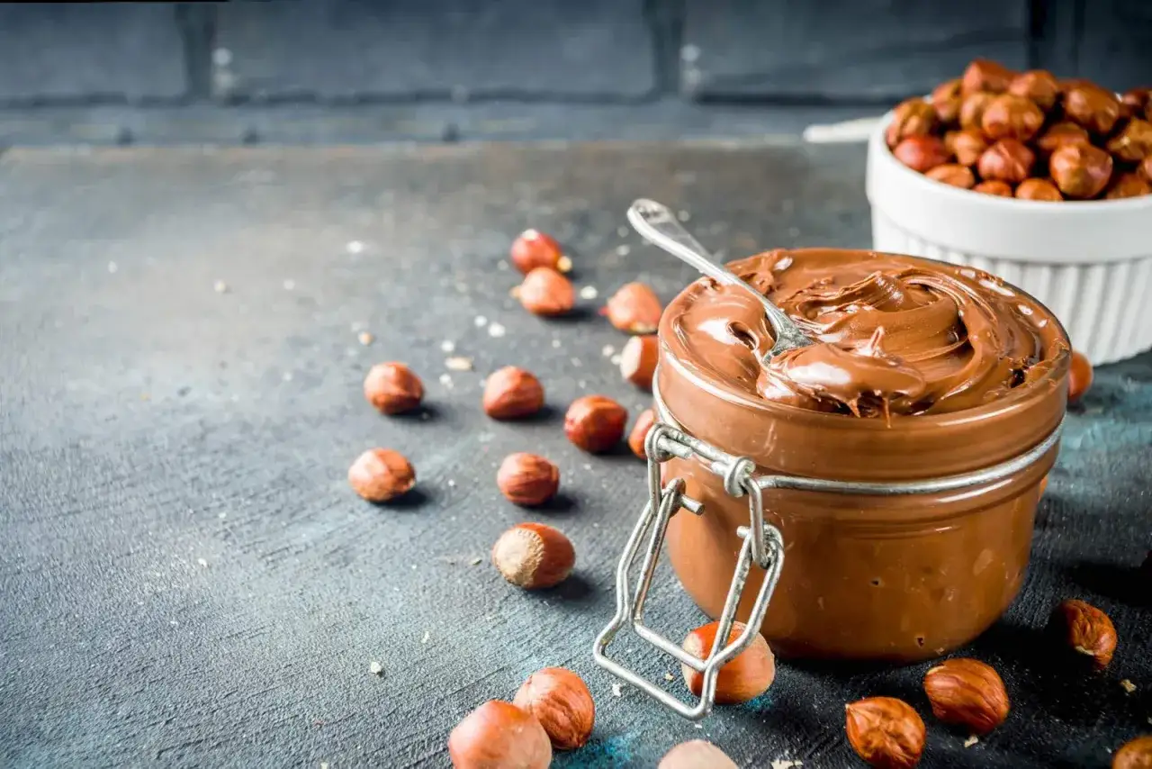 Crema di nocciole fatta in casa, cremosa e invitante, con nocciole sparse intorno.