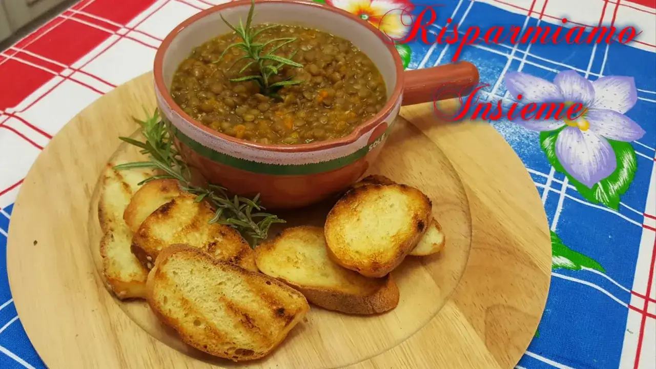 Una ciotola di zuppa di lenticchie veloce, guarnita con rosmarino, servita con crostini tostati su un tagliere di legno.