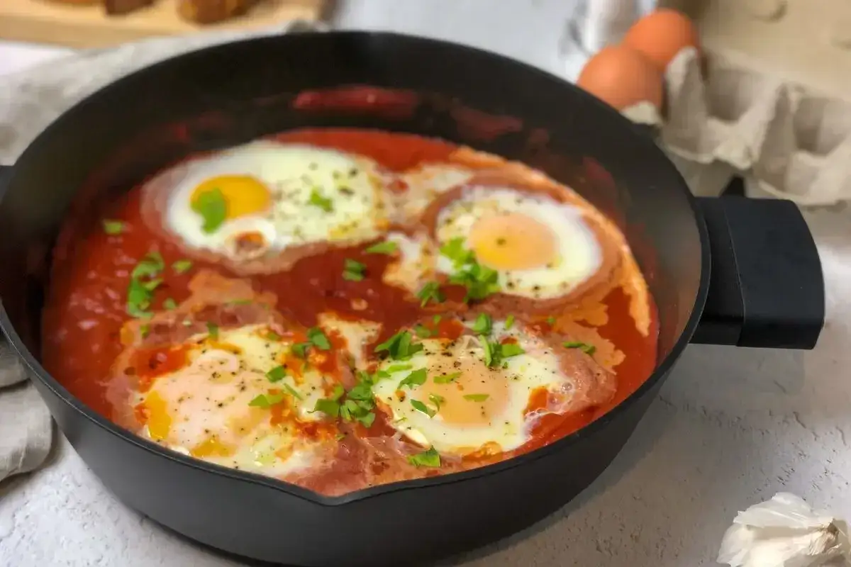 Uova al pomodoro cotte in padella, con tuorli morbidi e prezzemolo tritato. Un piatto semplice e gustoso.