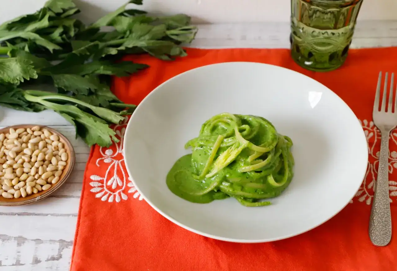 Un piatto di spaghetti verdi, conditi con una salsa cremosa e guarniti con gambi di sedano croccanti. Un'idea per ricette con foglie di sedano.