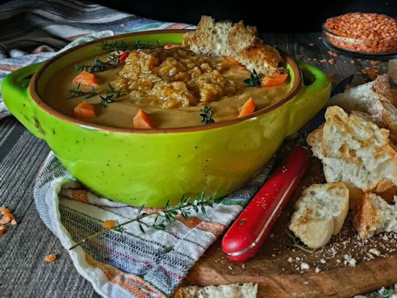 Una ciotola verde brillante piena di zuppa lenticchie rosse, guarnita con carote e timo, servita con pane croccante.