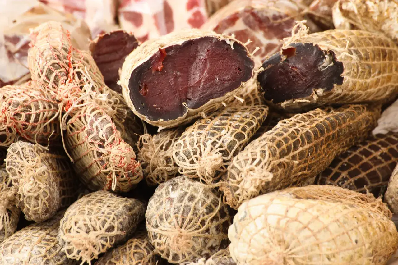 Un primo piano di bresaola, la bresaola che carne è, stagionata e avvolta in una rete.