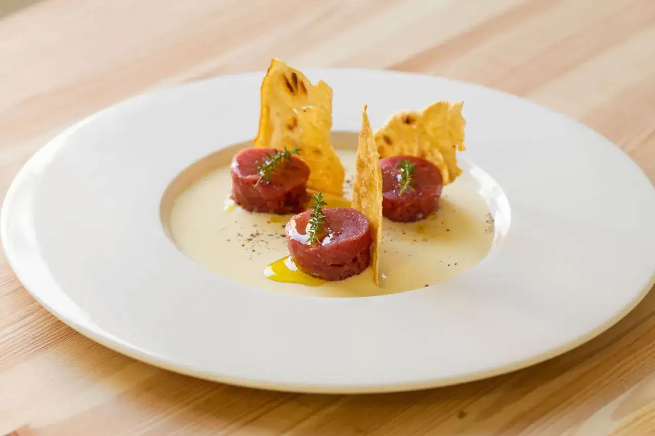 Tartare di manzo come condirla: tre cilindri di carne cruda su crema, guarniti con erbe aromatiche e croccanti sfoglie.