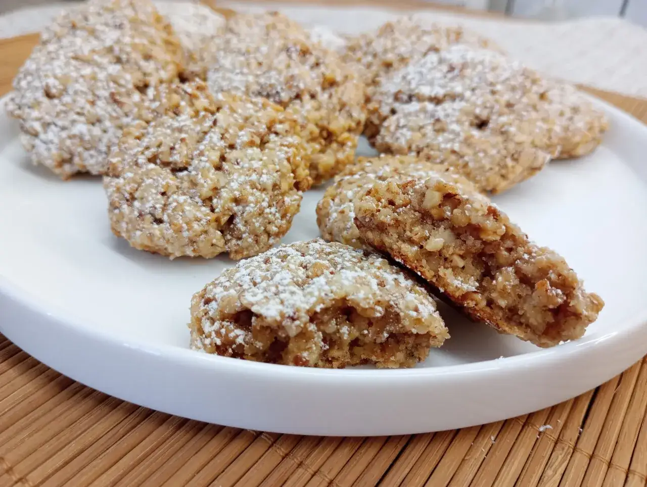 Biscotti con frutta secca, cosparsi di zucchero a velo, su un piatto bianco. Croccanti e invitanti, perfetti per una pausa golosa.