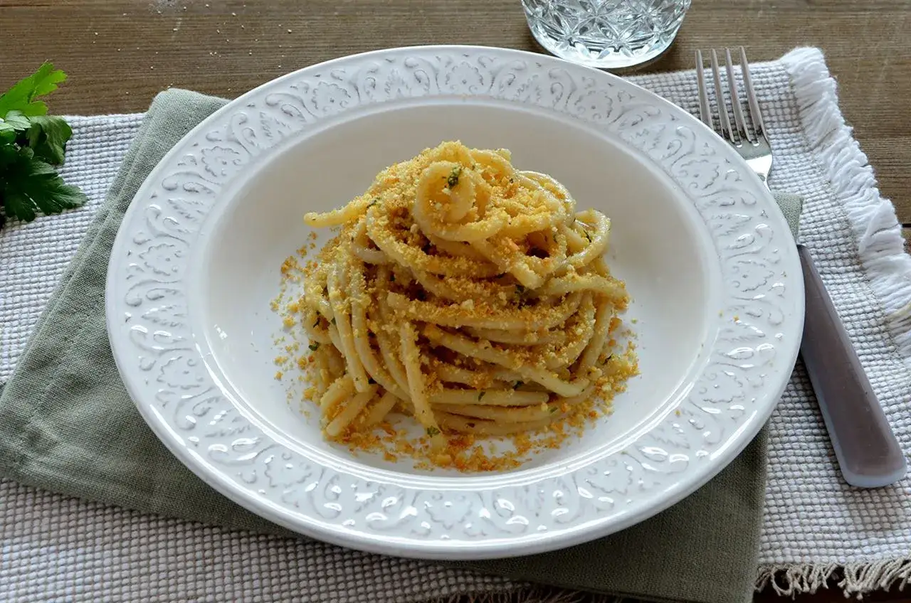 Pasta con pangrattato e acciughe alla siciliana, un piatto semplice ma gustoso, servito in un piatto bianco decorato.