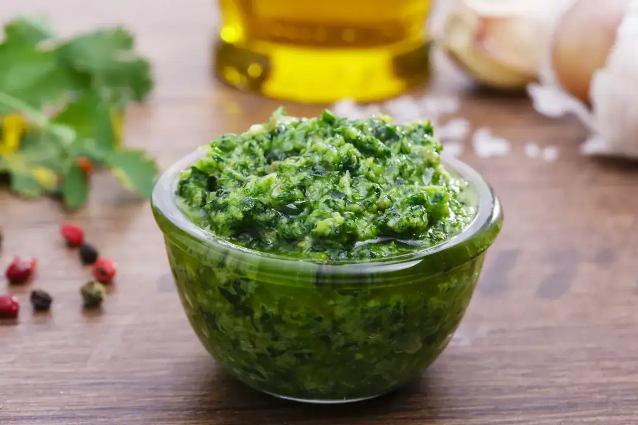 Salsa verde ricetta della nonna in una ciotola di vetro, con ingredienti freschi come aglio, olio e erbe aromatiche.