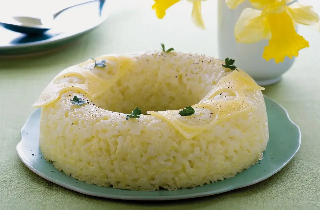 Sformato di riso a ciambella, guarnito con formaggio a fette e prezzemolo, su un piatto verde.