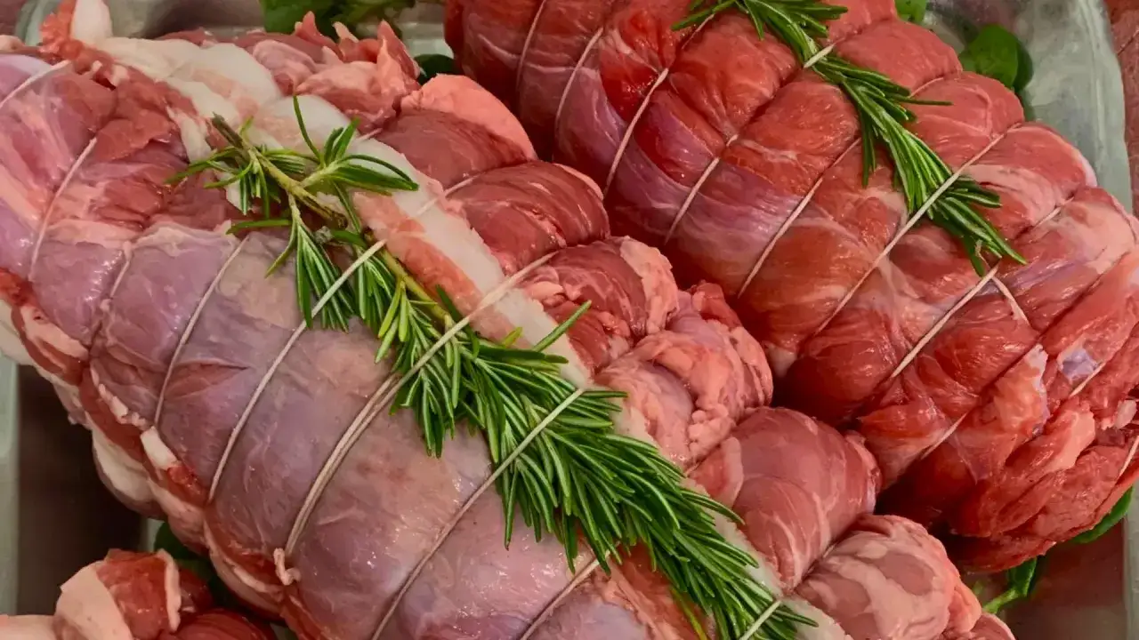 Due tagli di carne per arrosto pronti per essere cucinati, legati con spago e guarniti con rametti di rosmarino fresco.