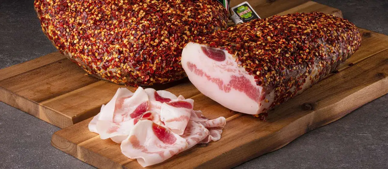 Guanciale, parte del maiale, ricoperto di peperoncino, su tagliere di legno.