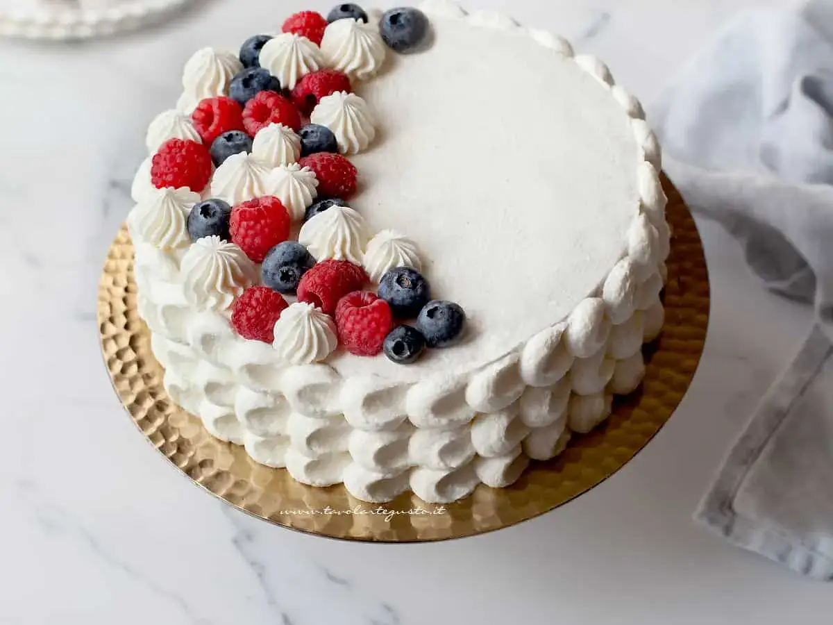 Delizioso pan di spagna torta con panna montata, lamponi e mirtilli freschi, decorata con ciuffetti di crema.