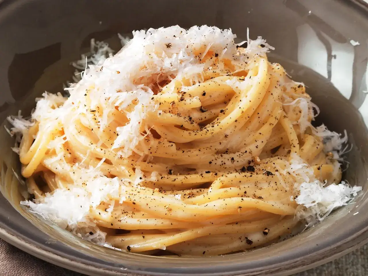 Un piatto invitante di spaghetti cacio e pepe, conditi con abbondante pecorino grattugiato e pepe nero macinato fresco.