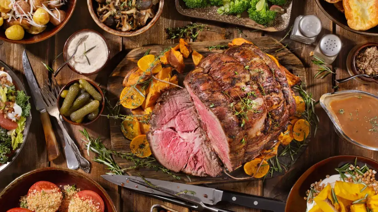 Il roast beef, che carne è? Un succulento arrosto di manzo, tagliato per mostrare la sua succosità, servito con patate dolci, arance e erbe aromatiche.